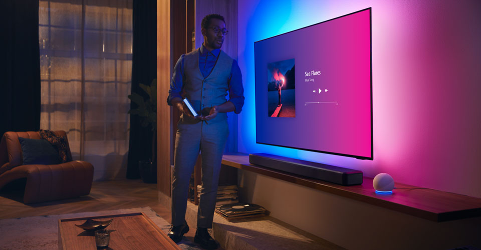 Žmogus modernioje svetainėje &scaron;alia &bdquo;Philips Ambilight&ldquo; televizoriaus su muzikos sąsaja ir &bdquo;Fidelio&ldquo; garso juosta